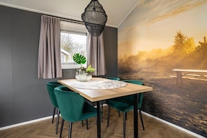 Ein Essbereich mit Tisch, Stühlen, einer Pendelleuchte und einem Wandbild mit Sonnenuntergangsmotiv.