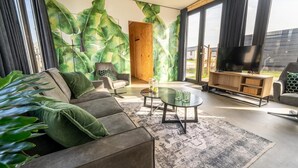 Moderni olohuone, jossa on sohva, sohvapöytä, televisio ja suuri ikkuna, jossa on verhot.