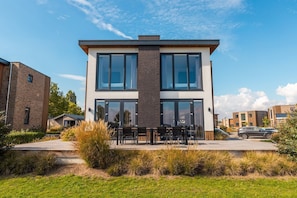 A modern two-story building with large windows, a patio with outdoor seating, and a well-maintained lawn.