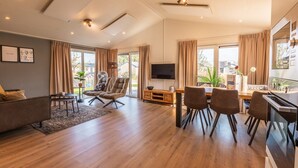 A modern living room with a sofa, chairs, a dining table, and a TV. - Vakantiepark Aan de Maas - Gelderse Lande | 6p (Kerkdriel)