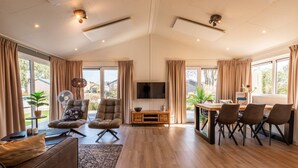 A spacious living room with a large TV, comfortable seating, and a dining area. - Vakantiepark Aan de Maas - Gelderse Lande | 6p (Kerkdriel)
