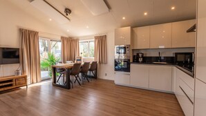 A modern kitchen with built-in appliances, a dining area with a table and chairs, and a TV mounted on the wall. - Vakantiepark Aan de Maas - Gelderse Lande | 6p (Kerkdriel)