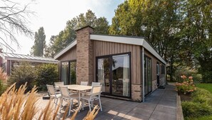 A modern house with a patio, a dining table with chairs, and a glass door leading to the interior. - Vakantiepark Aan de Maas - Gelderse Lande | 6p (Kerkdriel)