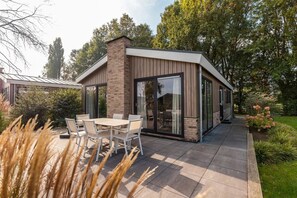 A modern house with a patio, a dining table with chairs, and a glass door leading to the interior.