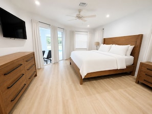 Ein Schlafzimmer mit einem Bett, Nachttischen aus Holz, einem Fernseher, einem Deckenventilator und Blick durch die Glastür.