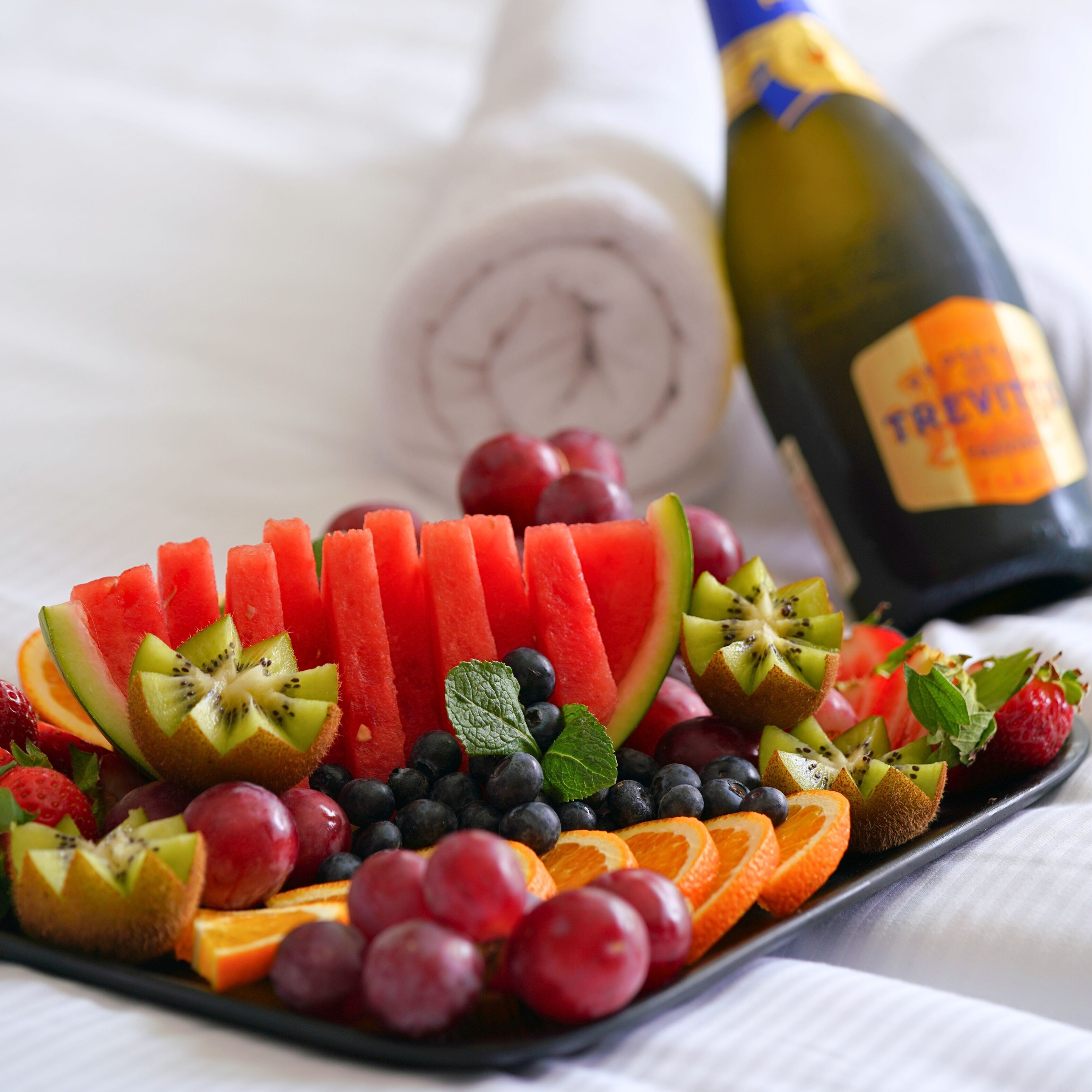 A fruit platter with various fruits and a bottle of champagne.