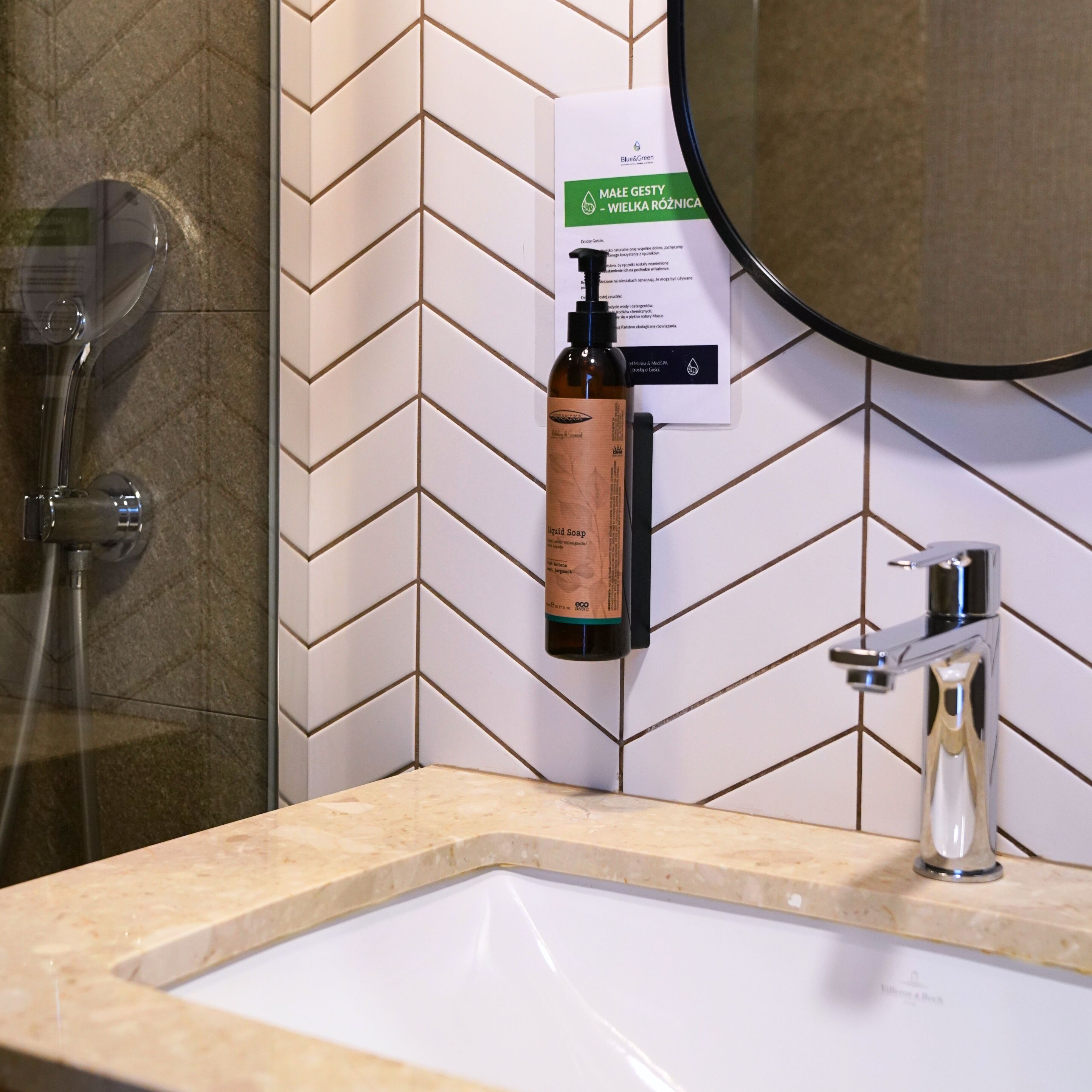 A bathroom with a herringbone tile backsplash, a sink, a mirror, and a shower.