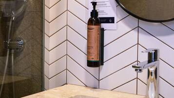A bathroom with a herringbone tile backsplash, a sink, a mirror, and a shower.