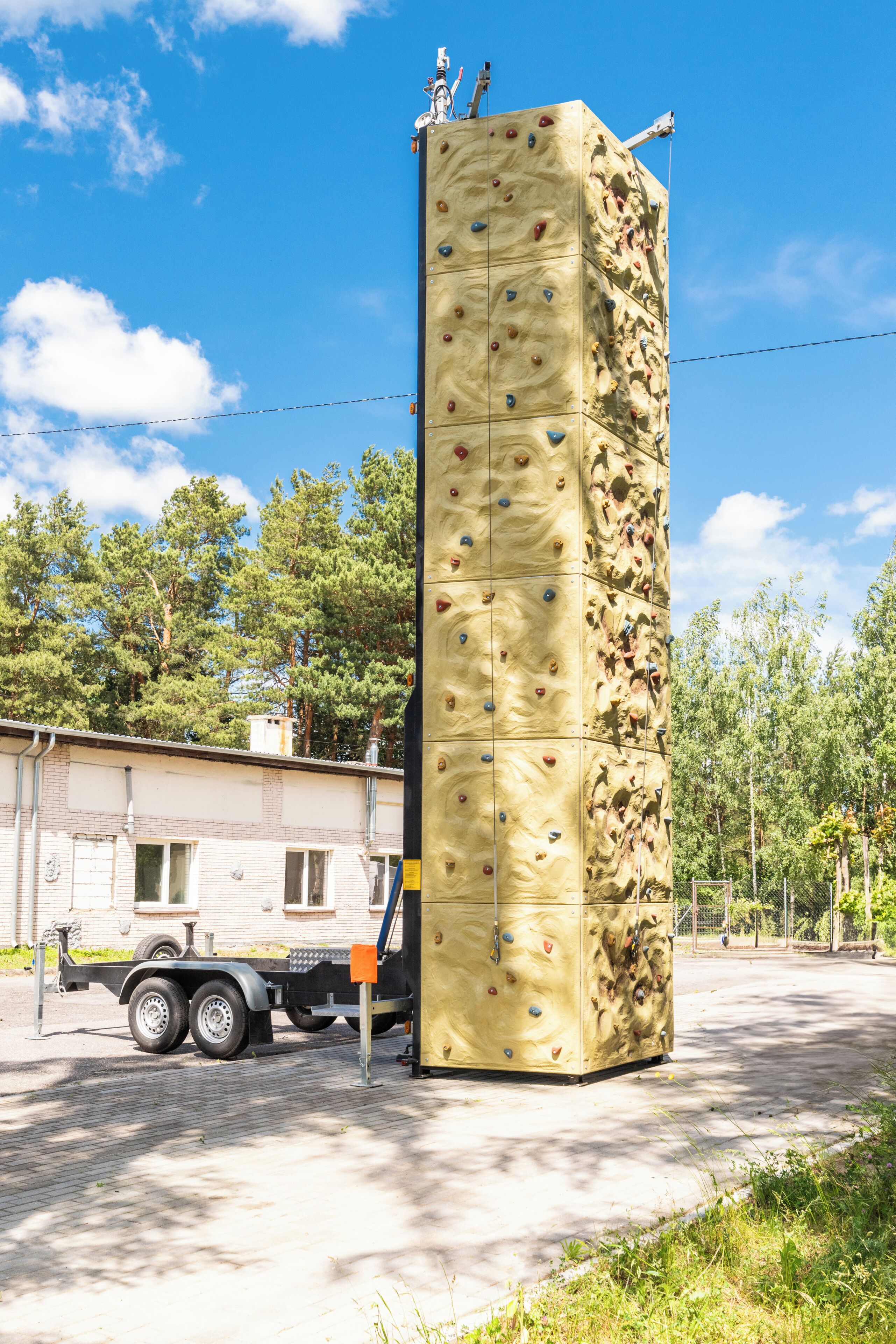 Una gran estructura de pared de escalada con numerosos puntos de agarre, una camioneta estacionada cerca y un edificio al fondo.