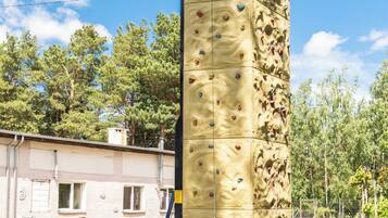 Una gran estructura de pared de escalada con numerosos puntos de agarre, una camioneta estacionada cerca y un edificio al fondo.