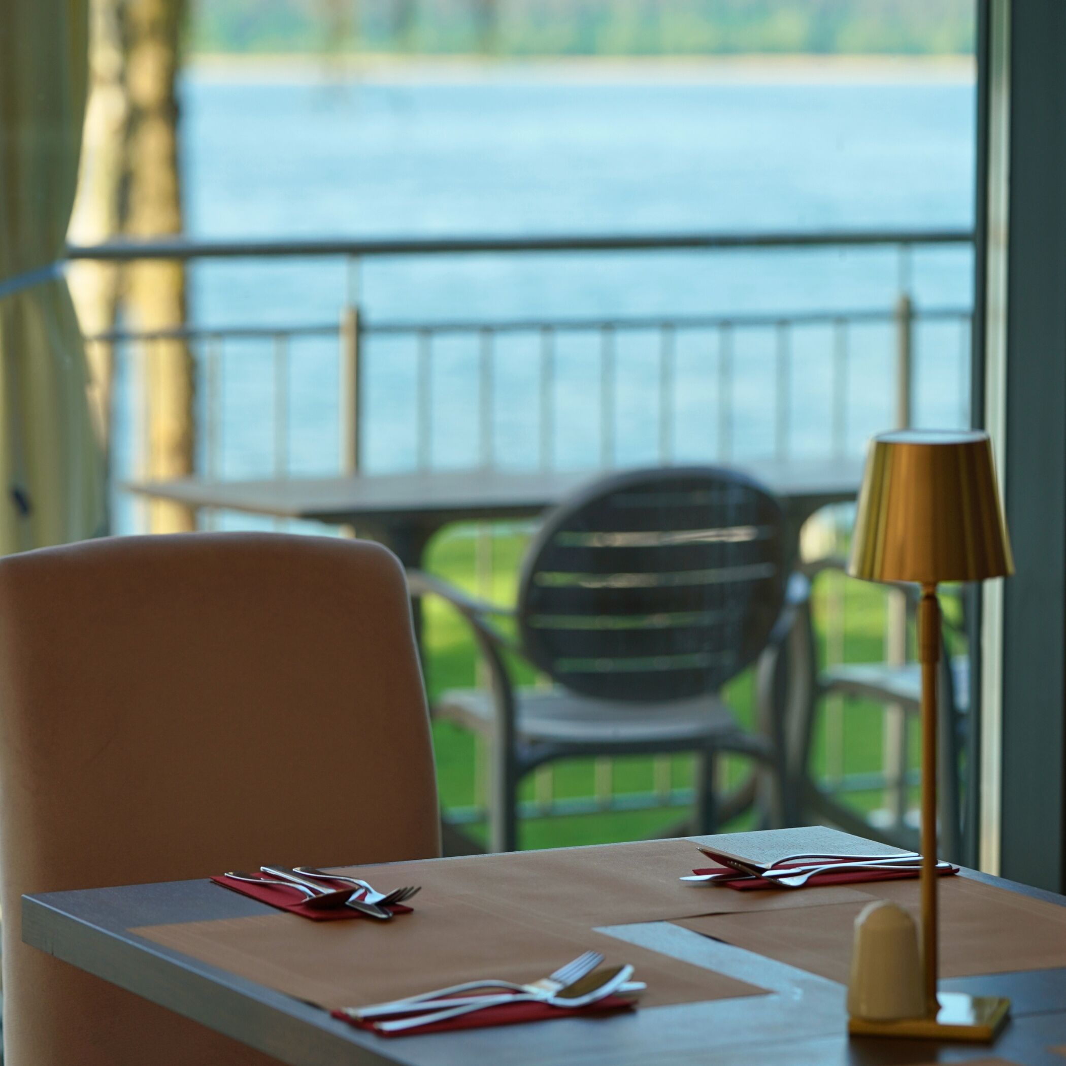 A dining table with chairs and a lamp, overlooking a body of water.