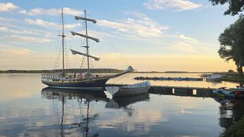 Un lago tranquilo con un barco de vela amarrado en un muelle, rodeado de aguas serenas y un cielo despejado.