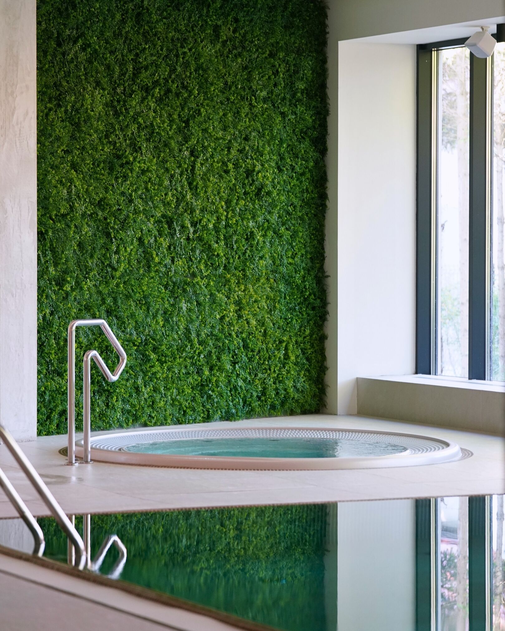 A modern indoor pool with a green wall and a clear glass barrier.