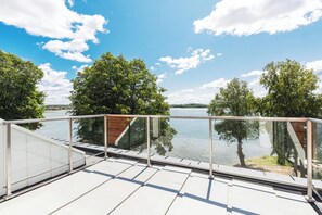 Barandilla de vidrio con vista a un lago tranquilo, árboles y cielo despejado.
