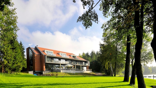 A modern building with a flat roof, large windows, and a balcony overlooking a grassy area.