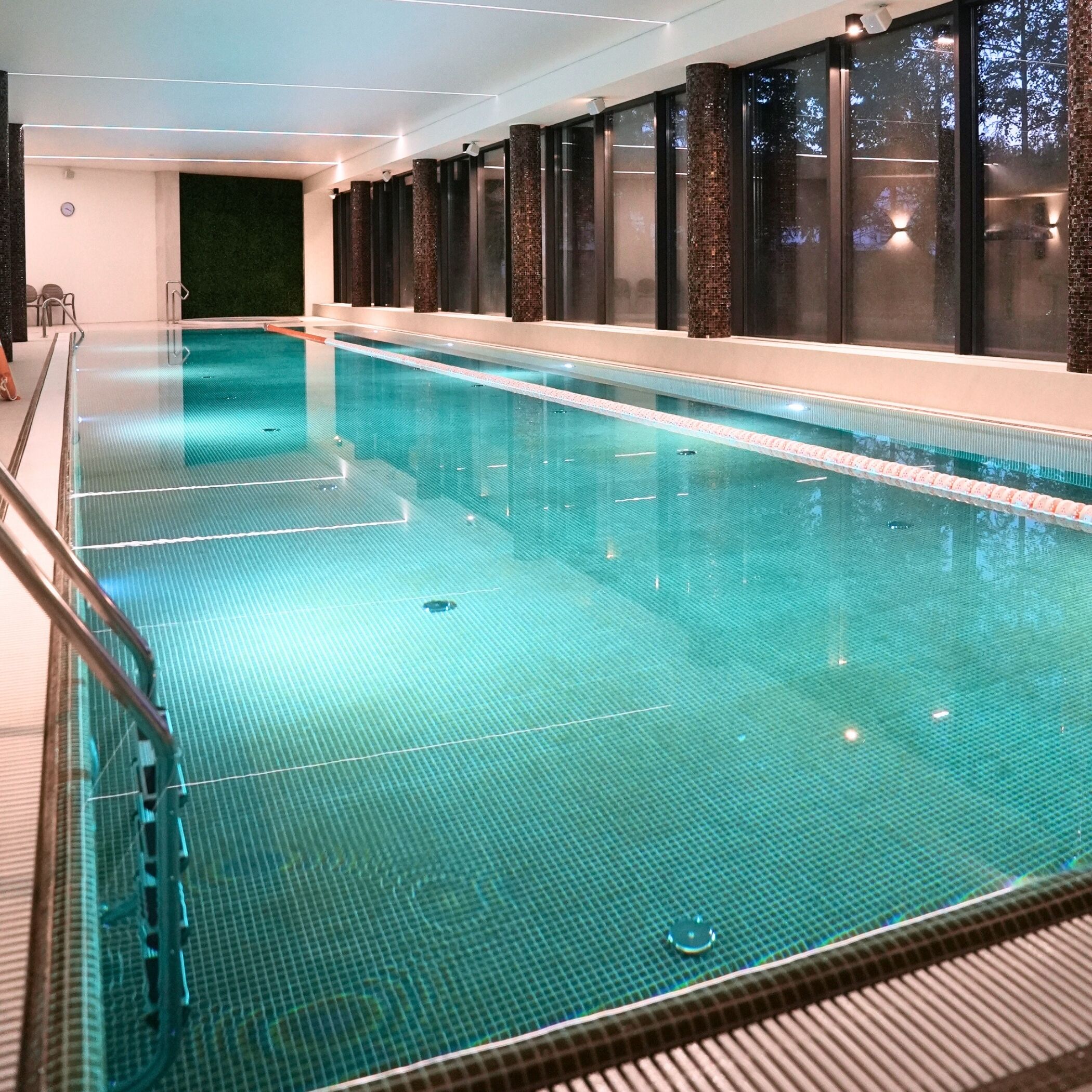 Una piscina con agua cristalina, rodeada de columnas oscuras y un muro de cristal.