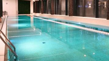 Una piscina con agua cristalina, rodeada de columnas oscuras y un muro de cristal.