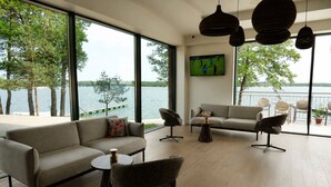 A modern living room with a large window overlooking a lake, furnished with sofas, chairs, and a coffee table.