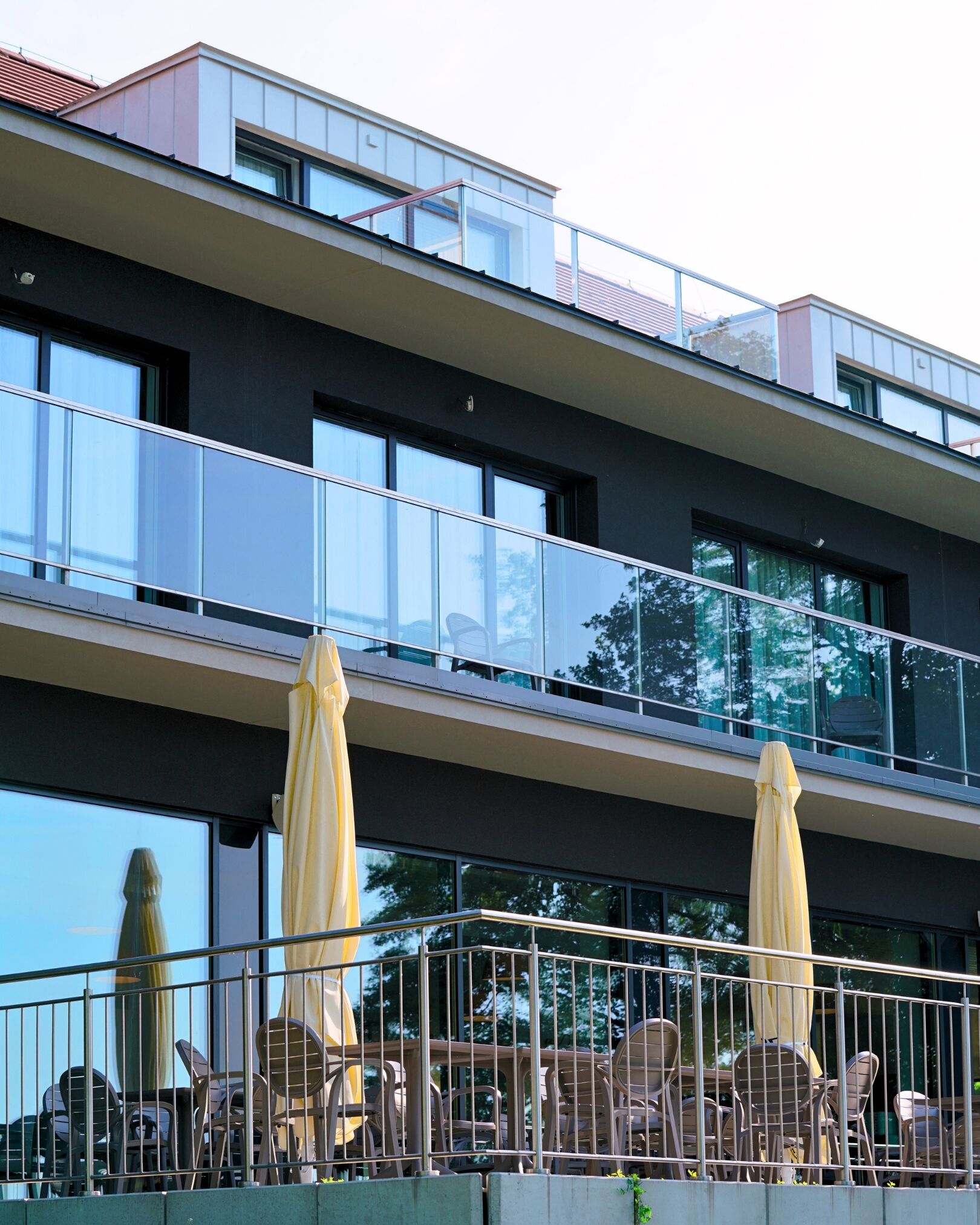 Ein modernes Gebäude mit Flachdach, großen Fenstern und Sitzgelegenheiten im Freien mit Sonnenschirmen.