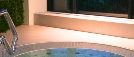 A hot tub with a metal faucet, a window with a view of a house, and a green wall.