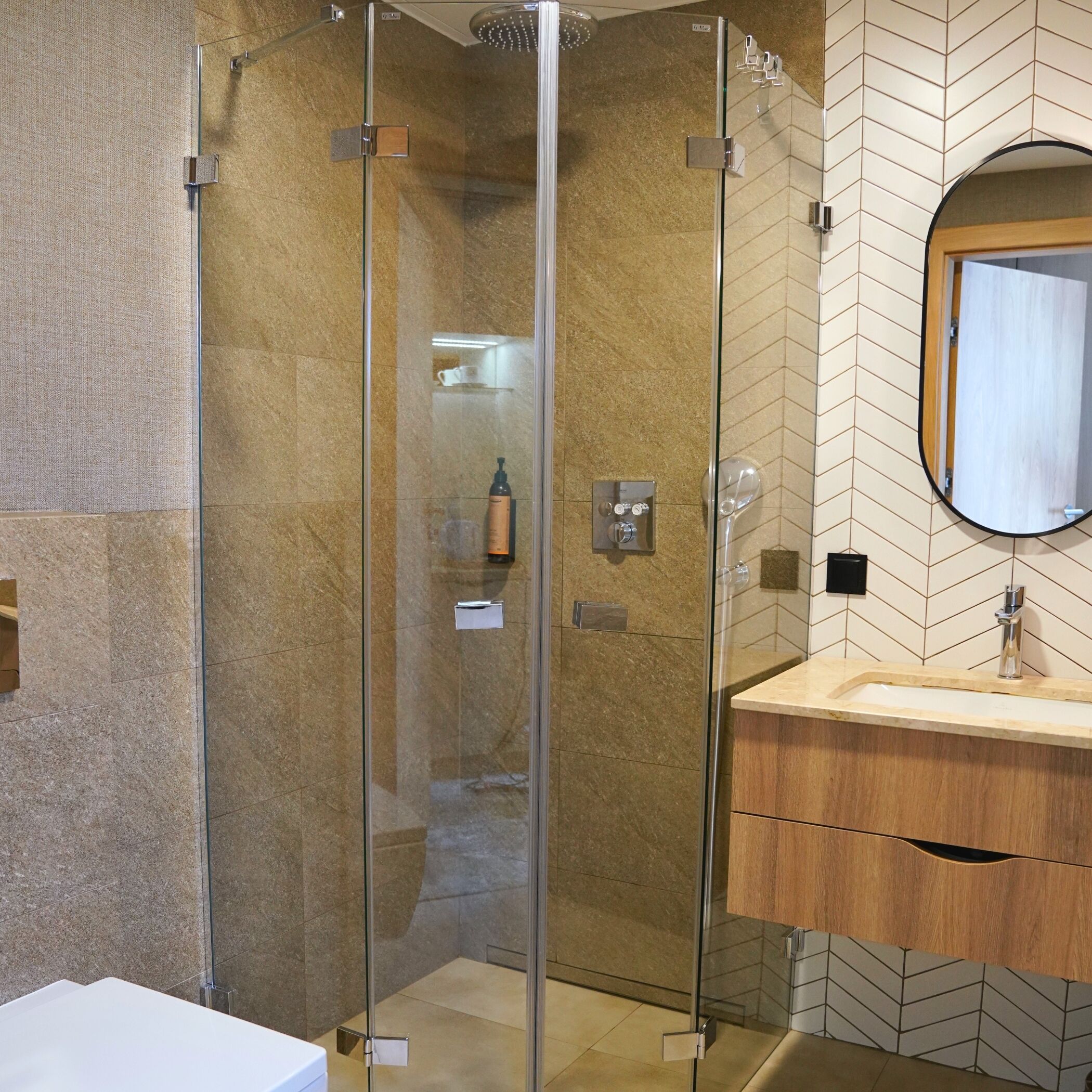 A modern bathroom with a glass-enclosed shower, a wooden vanity, and a herringbone-patterned tile backsplash.