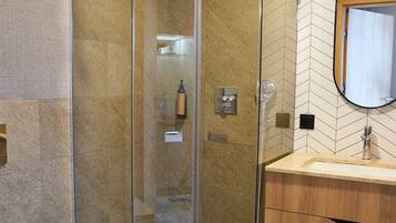 A modern bathroom with a glass-enclosed shower, a wooden vanity, and a herringbone-patterned tile backsplash.