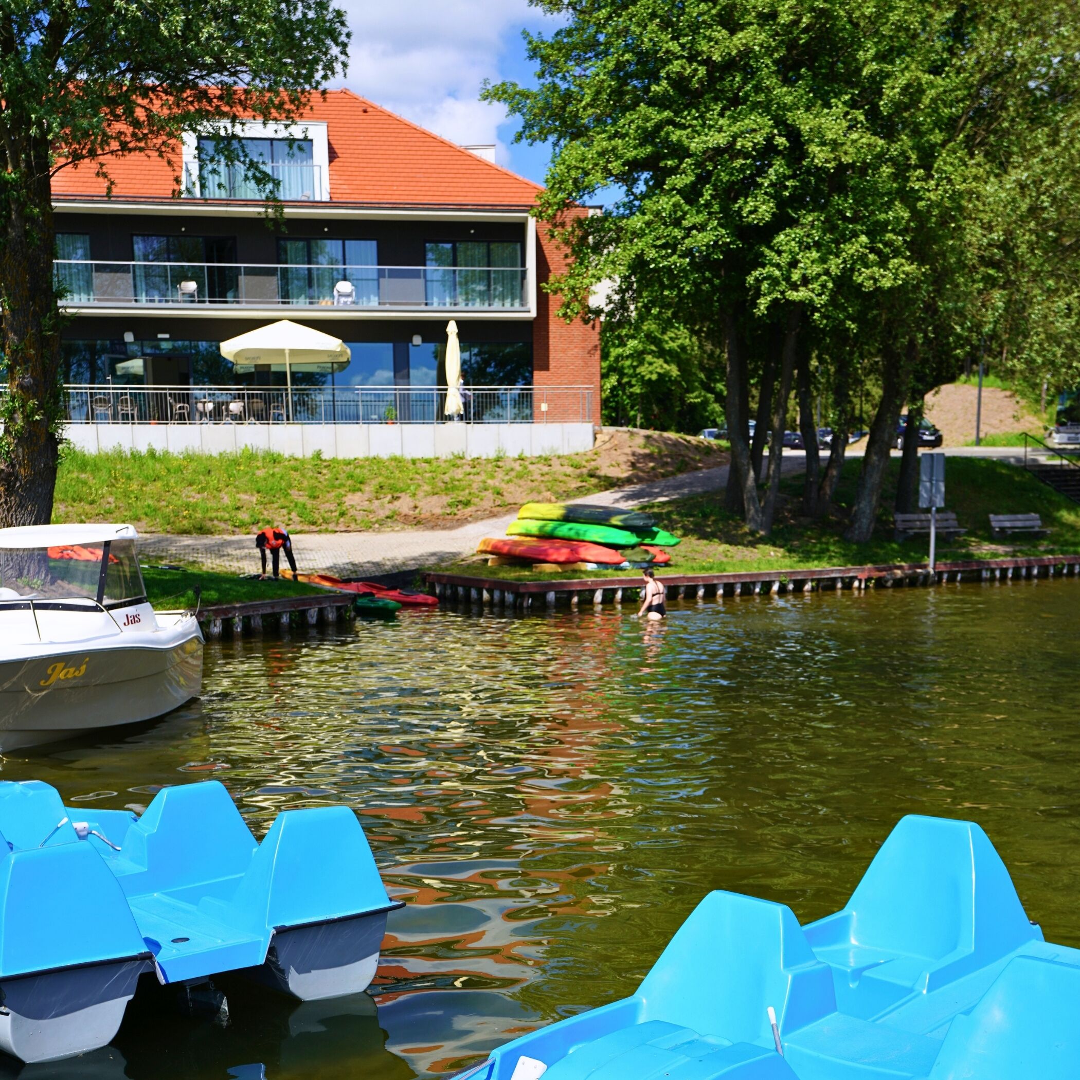 Vista a la orilla del río con un edificio, barcos y kayaks.