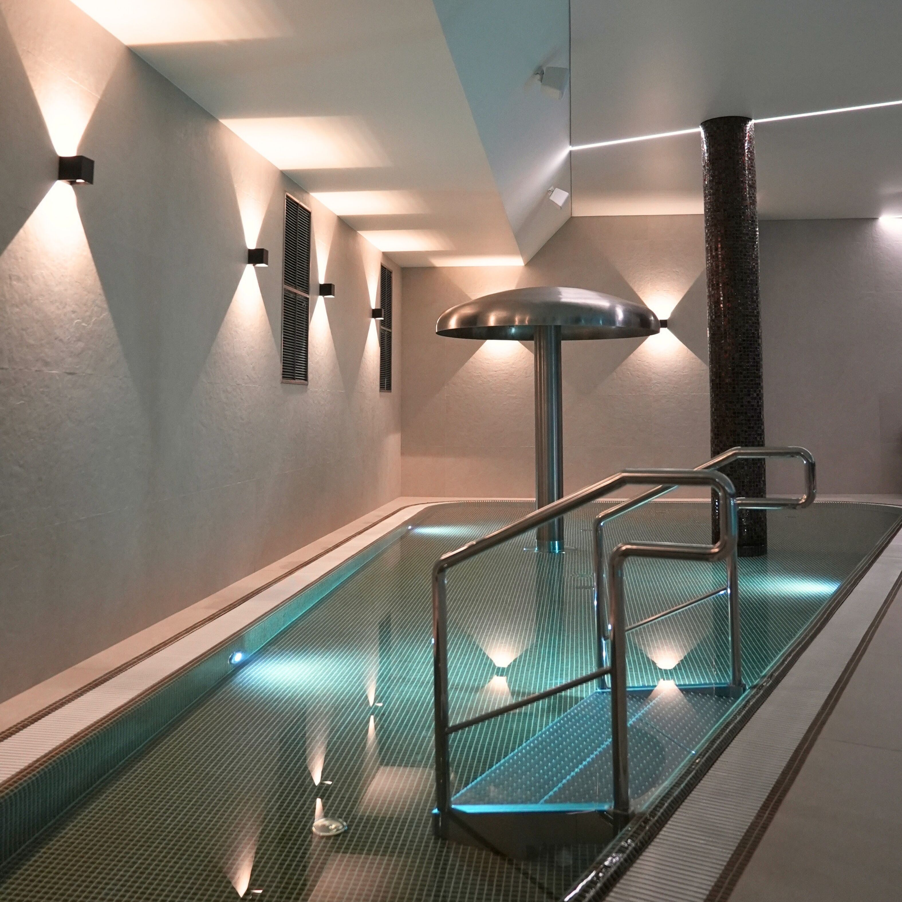 Una piscina interior con barrera de vidrio y pasamanos metálicos.