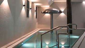 Una piscina interior con barrera de vidrio y pasamanos metálicos.