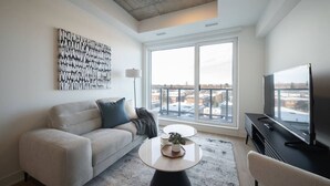 A modern living room with a sofa, coffee table, TV, and large windows.