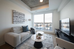 A modern living room with a sofa, coffee table, TV, and large windows.