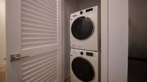 A laundry room with two stacked front-loading washing machines and a door with horizontal louvered panels.