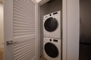 A laundry room with two stacked front-loading washing machines and a door with horizontal louvered panels.