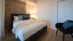 A bedroom with a bed, bedside table, lamp, chair, and a wardrobe.