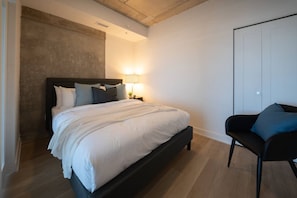 A bedroom with a bed, bedside table, lamp, chair, and a wardrobe.