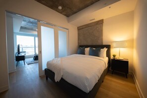 Een slaapkamer met een groot bed, een bureau en een stoel, een uitzicht door een glazen deur, en een plafond met zichtbare balken.