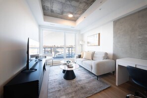Een moderne woonkamer met een flatscreen televisie, een bank, een salontafel en een uitzicht op de skyline door grote ramen.