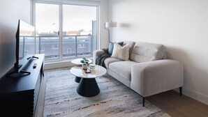 Ein modernes Wohnzimmer mit einer Couch, einem Couchtisch, einem Fernseher und einem großen Fenster.