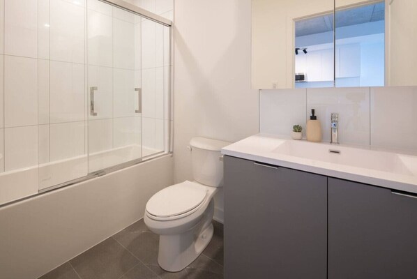 Un baño moderno con cabina de ducha de vidrio, inodoro y tocador con espejo.