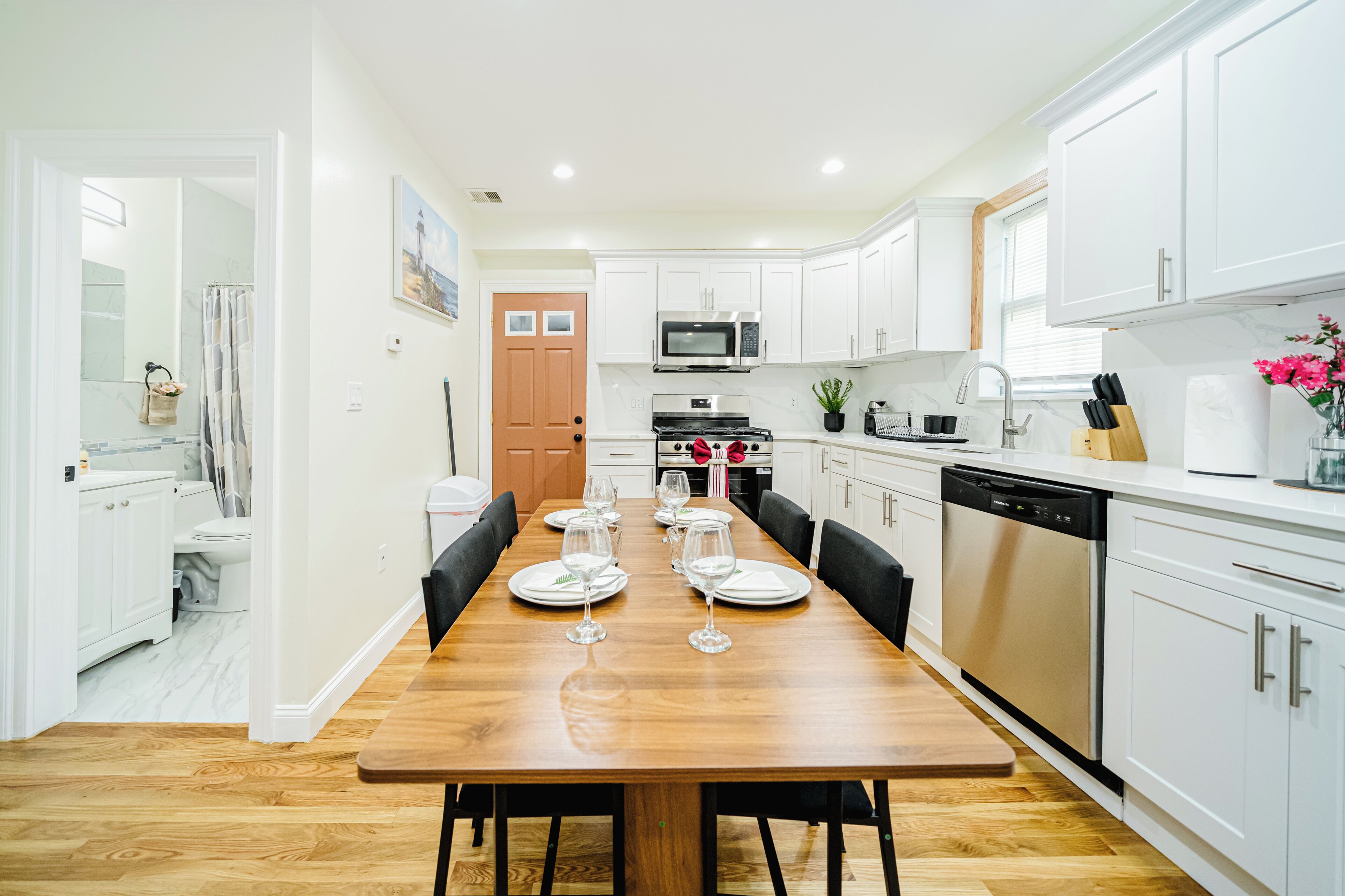 A modern kitchen with white cabinets, a wooden dining table set with plates and glasses, a microwave, oven, and dishwasher.
