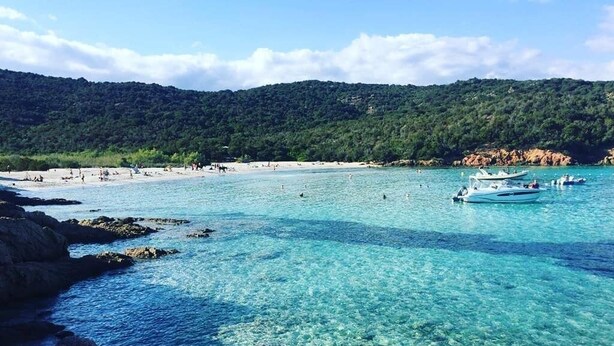 A coastal beach with clear water, boats, and a forested hill in the background. - Stone village house in the heart of nature and 15 minutes from the beaches (Conca)