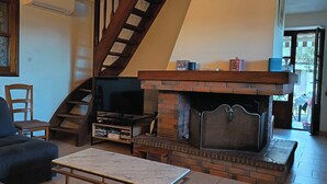 A living room with a fireplace, a sofa, a TV, and a staircase. - Stone village house in the heart of nature and 15 minutes from the beaches (Conca)