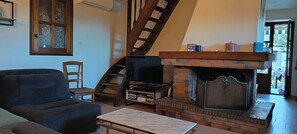 A living room with a fireplace, a sofa, a TV, and a staircase. - Stone village house in the heart of nature and 15 minutes from the beaches (Conca)