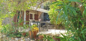 Un espacio de estar rústico al aire libre con pared de piedra, contraventanas de madera y plantas en macetas.