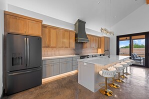 Eine moderne Küche mit Holzschränken, einem Edelstahlkühlschrank, einer zentralen Kochinsel mit Barhocker und einem großen Fenster.