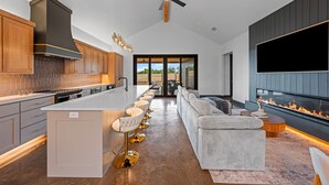 Una cocina moderna con una isla central, taburetes de bar y una pared con televisor grande.