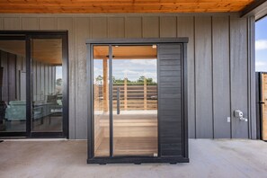 Une entrée moderne avec une porte coulissante en verre, une terrasse en bois et une vue sur un espace extérieur clos.