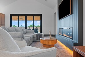 Un salon moderne avec un canapé d’angle, une table basse ronde et une cheminée.