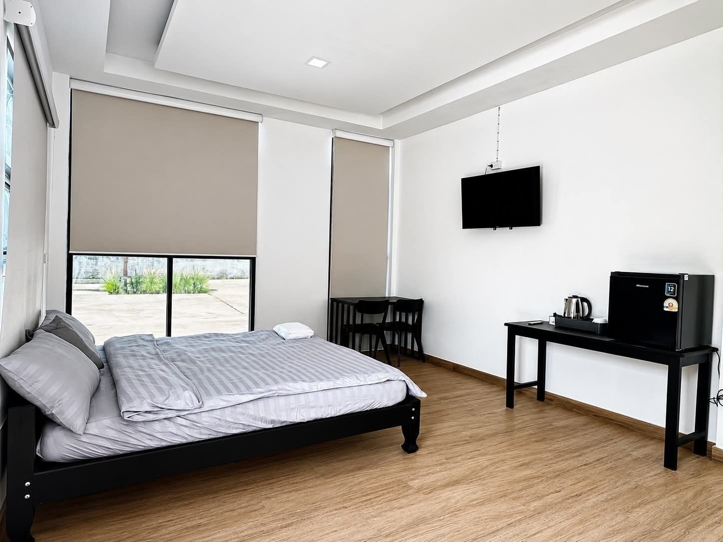 A modern bedroom with a bed, a desk, a television, and a window.