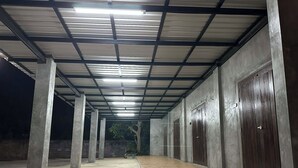 A covered corridor with concrete pillars, wooden flooring, and metal-framed ceilings.
